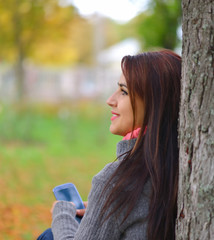 Beautiful girl messaging with phone in autumn park