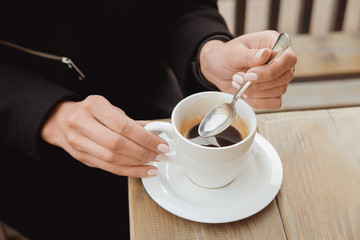 Hands with a spoon and a cup of black coffee