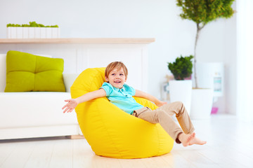 excited kid having fun, sitting on yellow bean bag at home