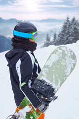 Fototapeta na wymiar Female snowboarder standing with snowboard in one hand and enjoying alpine mountain landscape - snowboarding concept