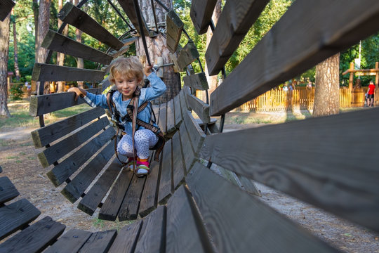 Little Girl Overcomes Obstacles. /  Three-year Girl The Blonde With A Personal Fall Arrest System Obstacle In The Rope Town.