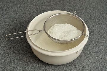 Fototapeta na wymiar Sifting flour into a white plastic bowl