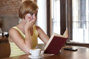 pretty woman enjoying reading book at coffee shop drinking cup of coffee or tea smiling happy