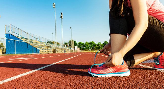 Female jogger tying her shoes on a stadium track - Powered by Adobe