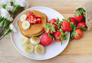 breakfast pancake with strawberry and slice of banana on whie pl