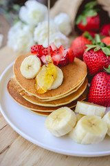 pour syrup on stack of pancake with strawberry and slice of bana