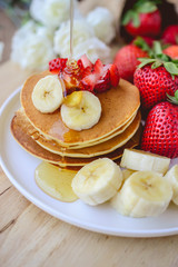 pour syrup on stack of pancake with strawberry and slice of bana