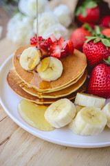 pour syrup on stack of pancake with strawberry and slice of bana