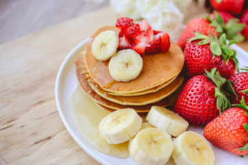 breakfast pancake with strawberry and slice of banana on whie pl