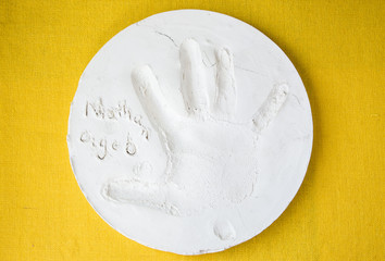 horizontal image of a round white clay plate with a small child's hand print pressed into it on a yellow background.