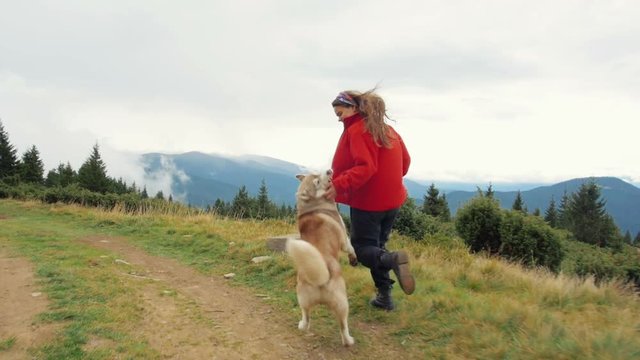 Young female playing and running with siberian husky dog in mountains, slow motion