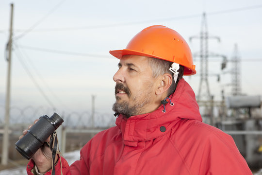 Engineer at Electrical Substation looks through a binoculars