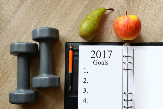 Dumbbells with fruits and open notebook on wooen desk. Healthy resolutions for the New Year 2017.