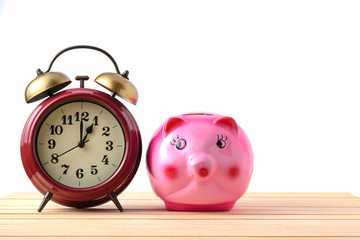 Piggy bank and retro clock on a wooden floor with a white backgr