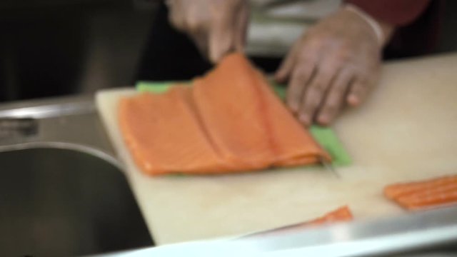 Process of making and cutting salmon for sushi rolls. Cook cutting up fish by knife on thin slices.