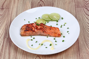 Grilled salmon topped minced shallot ,mayonnaise and sliced lemon on white dish. Isolated.