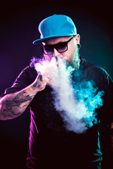 Men with beard  in sunglasses vaping and releases a cloud of vapor.
