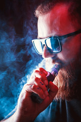 Men with beard  in sunglasses vaping and releases a cloud of vapor.