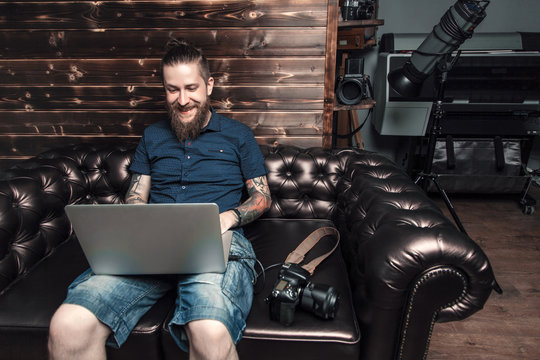 Beautiful portrait of the photographer at the workplace. The concept of the creative process, skill and favorite pastime. Male boss sitting on the couch in his office, working on laptop