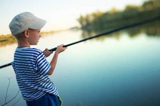 little boy in a cap fishes a fishing tackle in the river in summer