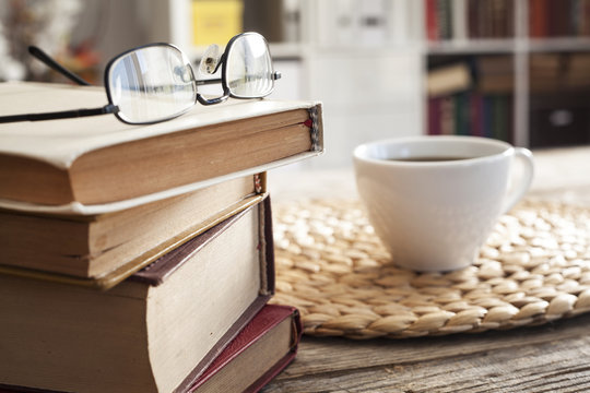 Pile of books with reading glasses on desk