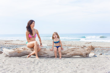 Beautiful brown haired woman sitting on the beach with her blonde child