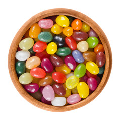 Jelly beans in wooden bowl on white background. Assorted small bean-shaped sugar candies in different colors with soft candy shells and gel interiors. Isolated macro food photo close up from above.