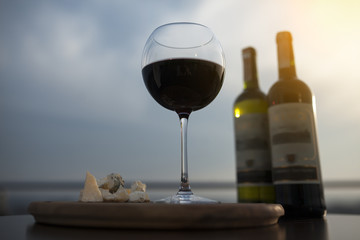 two bottles of red french wine with wineglass and cheese;