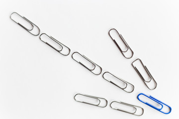 Metal paperclips in the shape of arrow down, blue on the top, isolated on white background. Business concept, high angle, flat
