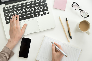 Hand working on a laptop, another holding a pen ready to write in the notebook. Business concept, high angle - Powered by Adobe