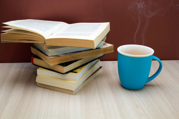 Fototapeta na wymiar a stack of books and a hot drink in a blue mug on wooden table,