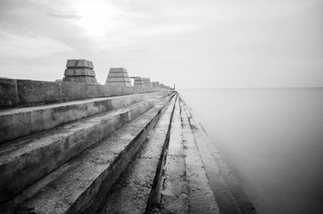 black and white image, wave hitting concrete jetty or pier on th