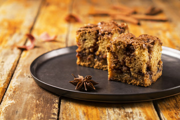 Cinnamon zucchini coffee cake on a black plate on a worn wooden light background with red dry leaves. Selective focus 