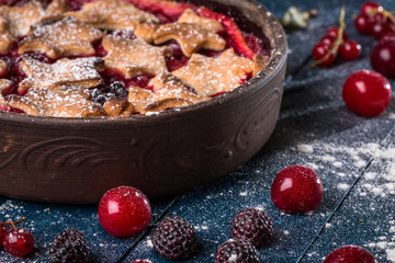 Berry pie decorated with stars, sugar powder and berries on the navy-blue background 
