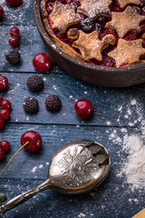Berry pie with stars decorated with berries, spoon and sugar powder on the navy blue background