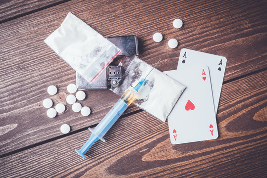 Hard drugs with pills, playing cards and syringe on wooden table