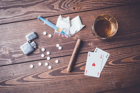 Hard drugs with pills, playing cards, syringe and alcohol on wooden table