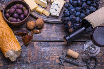 Fototapeta na wymiar Red wine in a bottle and a set of products - cheese, olives, bread, nuts, figs on a wooden board, background