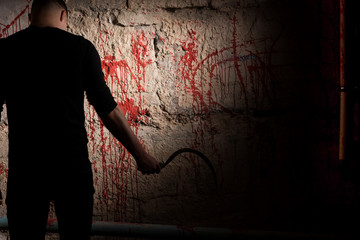 Shadowy male figure holding sickle near blood stained wall