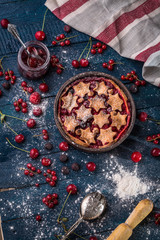 Berry pie decorated with stars, jam, sugar powder and berries on the navy-blue background with kitchen towel