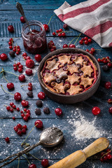 Berry pie with stars decorated with berries, spoon, rocker, towel and sugar powder on the navy blue background