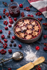 Berry pie decorated with stars, jam, sugar powder and berries on the navy-blue background with kitchen towel