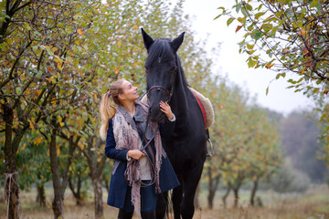 Beautiful stylish girl in a cowboy hat with a horse walking in the autumn forest, country style