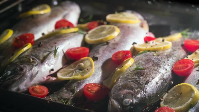 delicious trout fish is baking in the oven with lemon, tomatoes and spices