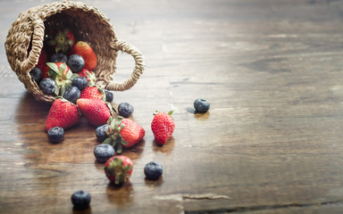 Mix of fresh strawberry and blueberry in a basket on rustic wooden background.