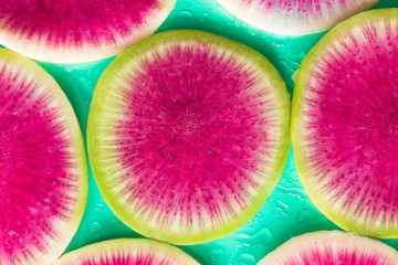 Obraz na płótnie Canvas Slice of radish with a pink pith. Green background. Drops of wat