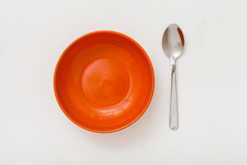 top view of orange bowl and spoon on white plaster