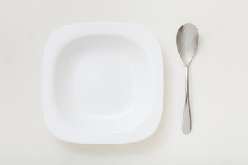 top view of square white bowl and spoon on plaster