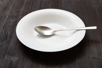 white deep plate with spoon on dark brown table