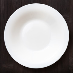 above view of white deep plate on dark brown table